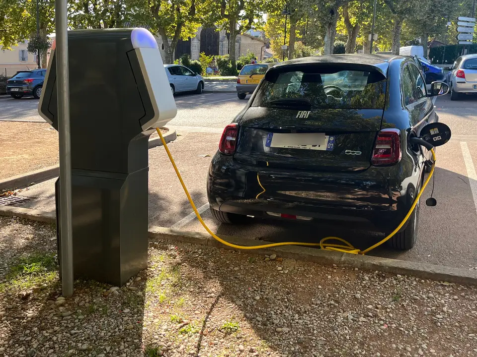 Une petite voiture électrique branchée sur une borne, sur un parking de Montluel, dans l'Ain